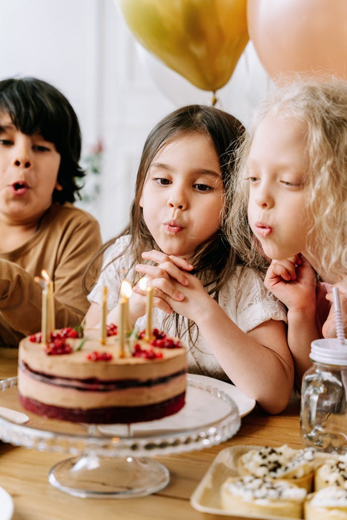 Children having fun blowing out candles on a birthday cake indoors.