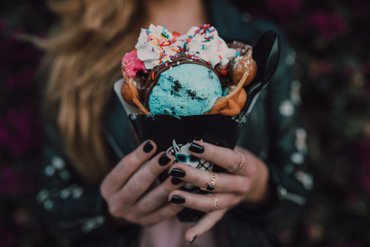 Close-up of a vibrant bubble waffle and ice cream dessert held by a woman.